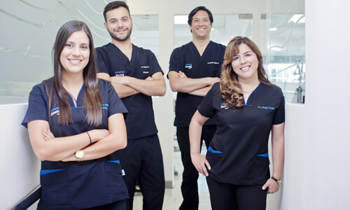 Picture of a dental team representing the dental services of the Costa Rica Dental Centre in San Jose, Costa Rica.  The team consists of 2 male dentists and 2 female dentists, who are wearing dark blue work uniforms.