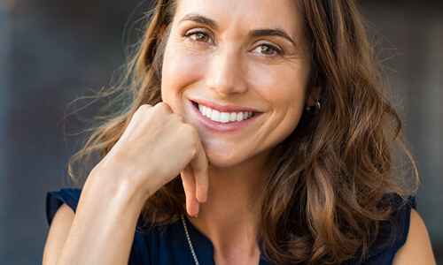 Picture of a smiling woman, happy with the cosmetic dental treatments she had at the Costa Rica Dental Centre in San Jose, Costa Rica.  The woman has long brown hair and is wearing a black blouse.  She has perfect teeth and is smiling directly at the camera.